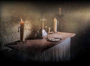 A cross sits between two lit candles on an rustic communion table.